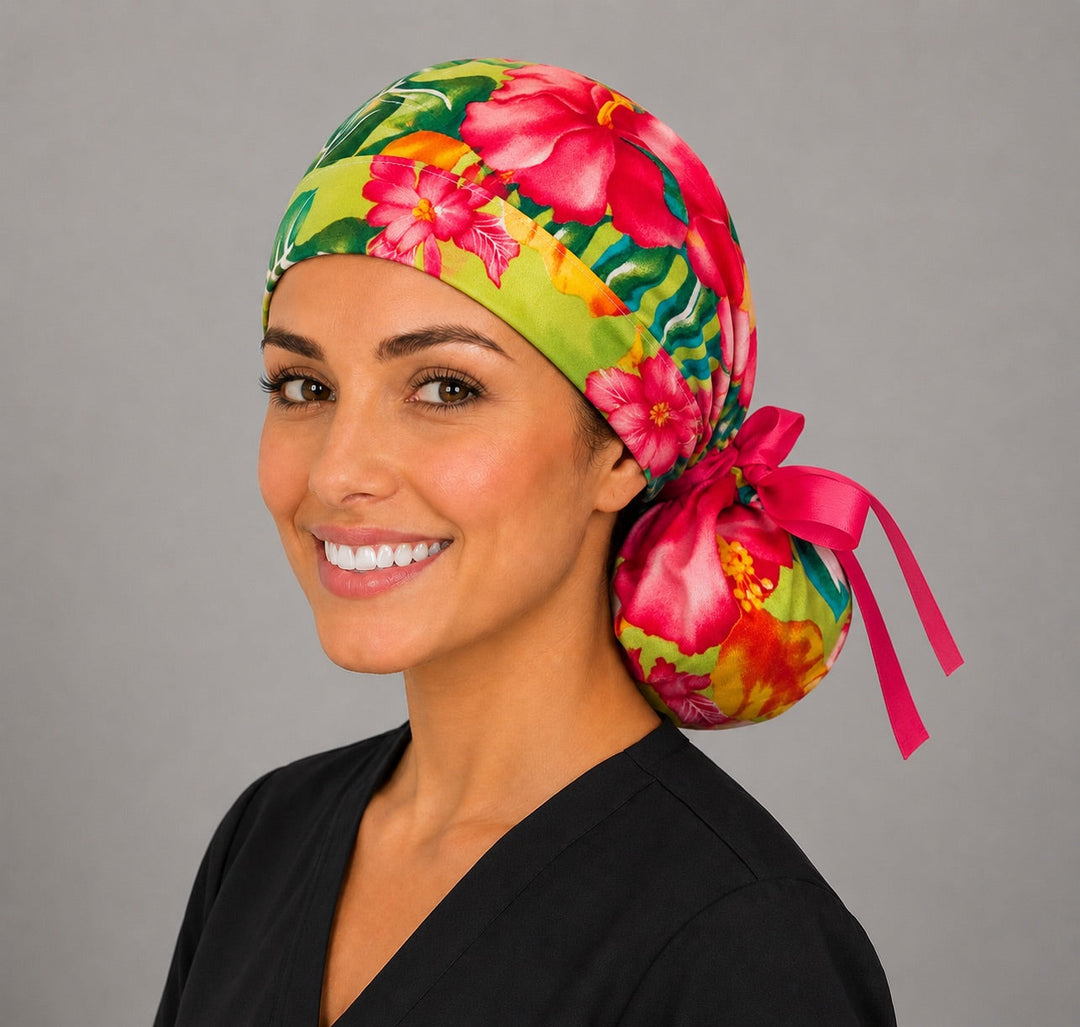 Tropical hibiscus ponytail scrub cap on a smiling woman, vibrant pink and orange flowers on green foliage with a hot pink ribbon bow and back pouch for long hair, handmade in USA surgical hat for women, OR World