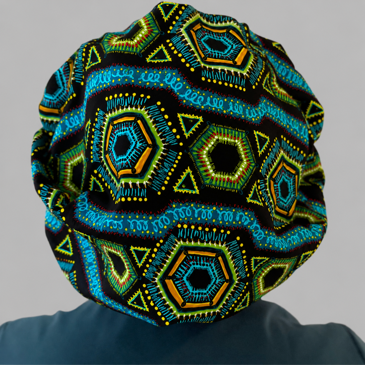 Nurse wearing Colorful Spirit African print bouffant scrub cap black background teal green gold geometric pattern surgical hat handmade OR World back view 