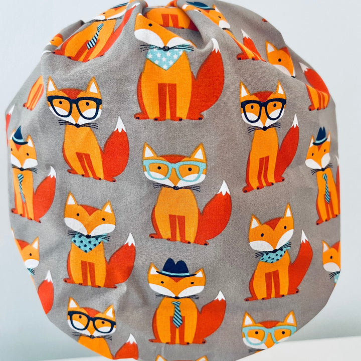 Cute fox bouffant scrub cap print detail, orange foxes in glasses, bow ties and hats on gray cotton, women&