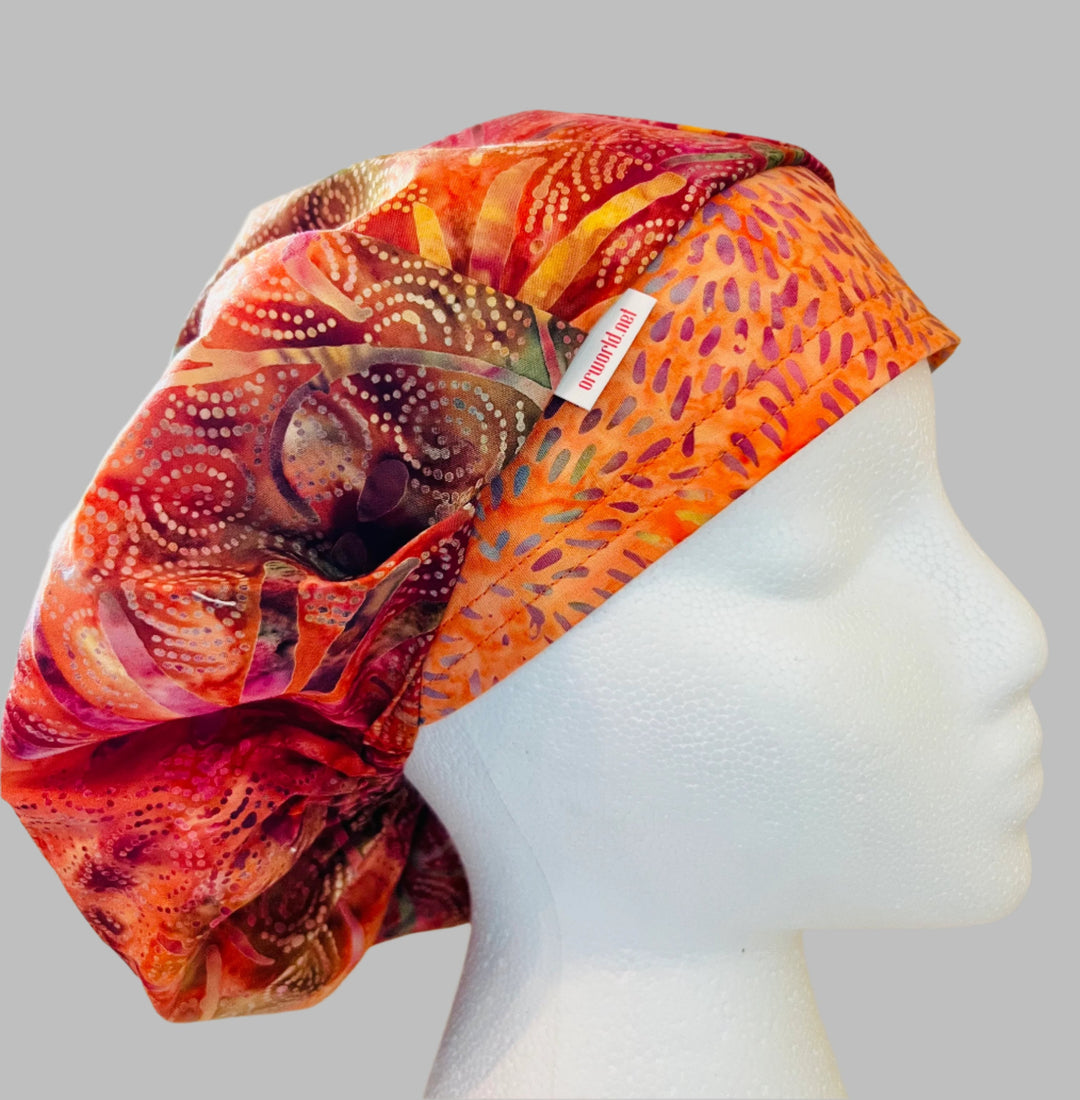 Top view of colorful pink &amp; orange batik bouffant scrub cap — handmade-in-USA surgical hat, bright gift for nurses &amp; surgeons.