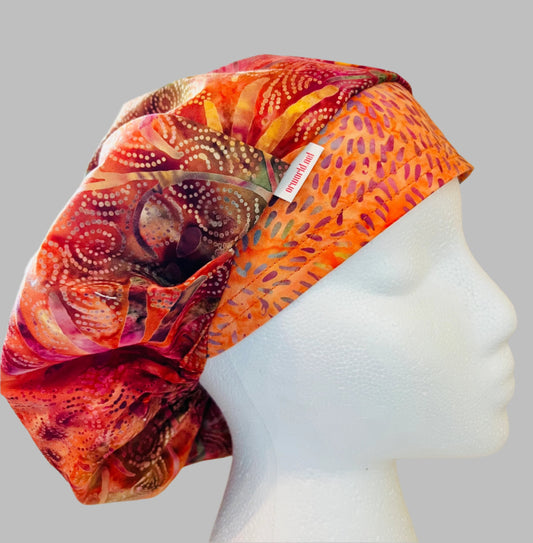 Top view of colorful pink & orange batik bouffant scrub cap — handmade-in-USA surgical hat, bright gift for nurses & surgeons.