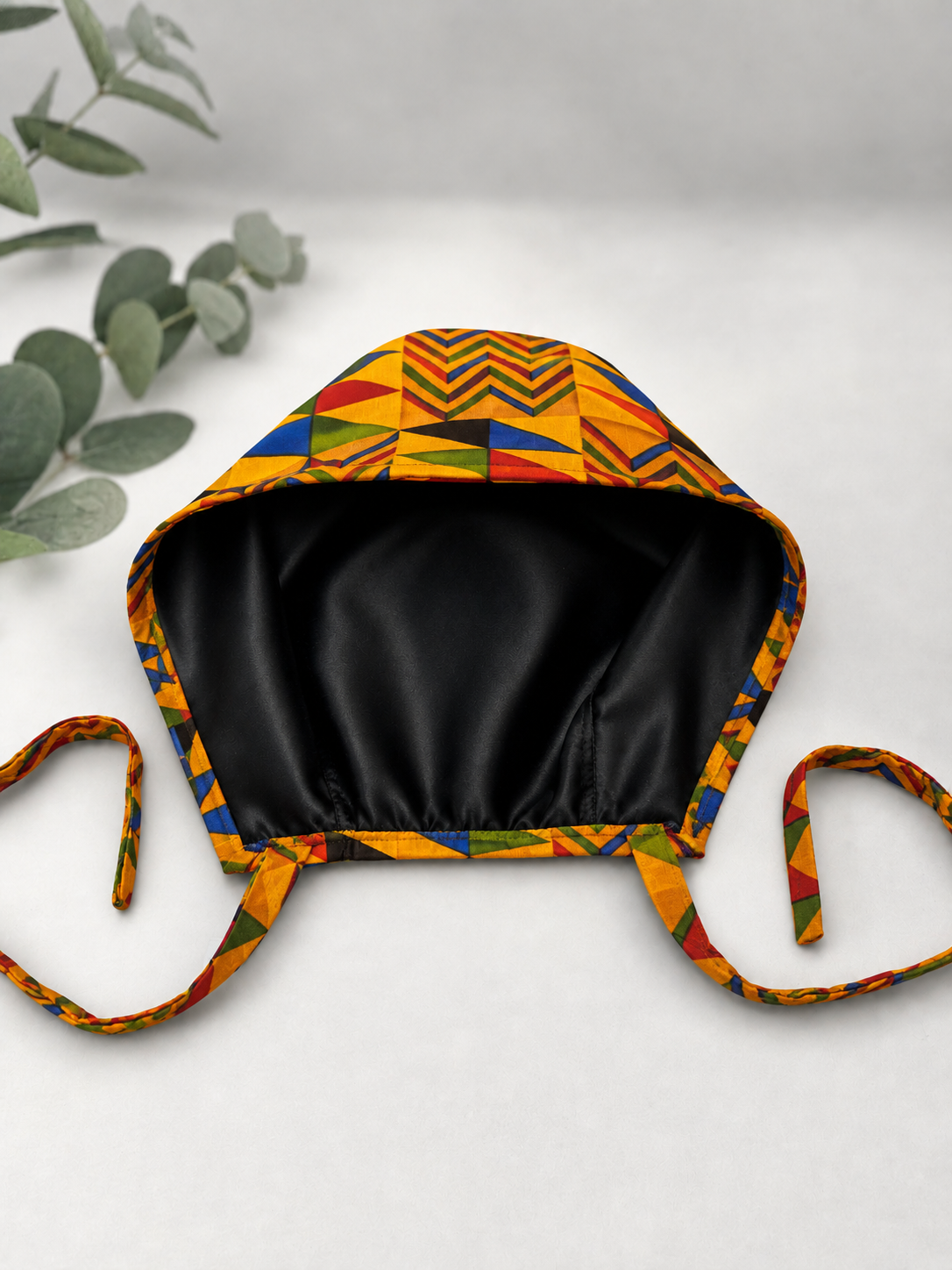 Colorful Geometric African Kente mens tieback scrub cap flat lay showing black satin lining interior bold Ghana triangle pattern surgical hat handmade USA OR World