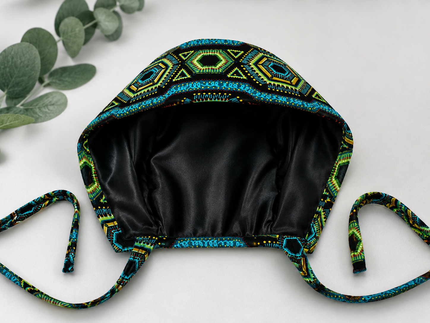 Colorful Spirit African Kente mens tieback scrub cap flat lay showing black satin lining interior bold black teal green gold geometric pattern surgical hat handmade USA OR World