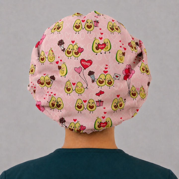 Back view of the avocado heart bouffant scrub cap — full roomy fit showing avocado couples, Love hearts and gifts on a blush pink print