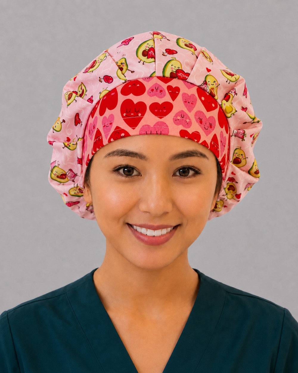 Woman wearing an avocado Valentine bouffant scrub cap, front view — smiling avocado couples and heart balloons on blush pink with red heart band, adjustable women's surgical hat