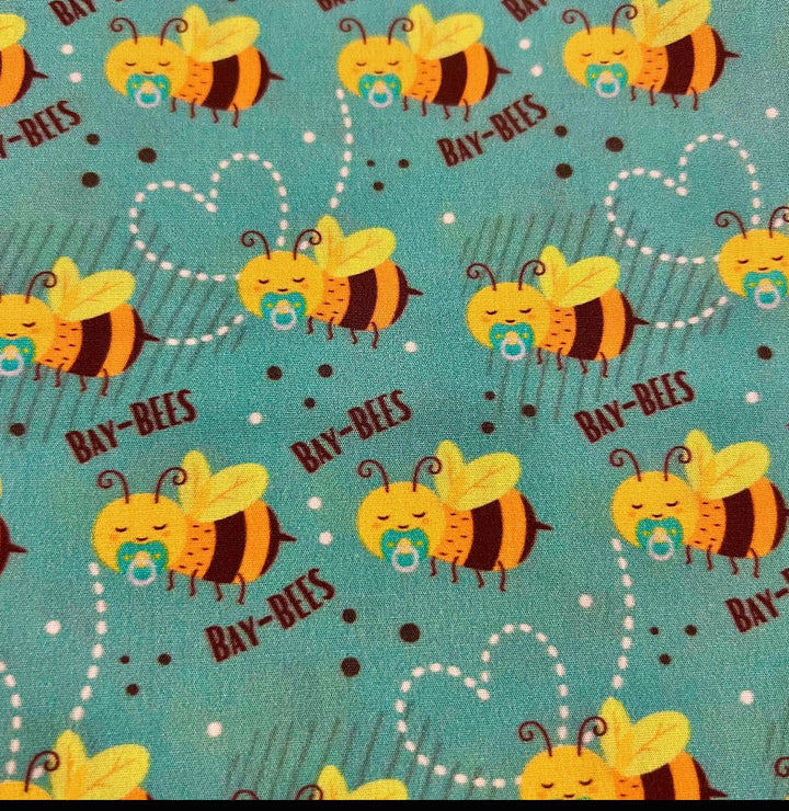 Fabric detail of the Bay-Bees scrub cap — close-up of sleeping honeybees with pacifiers and dotted heart trails on teal cotton