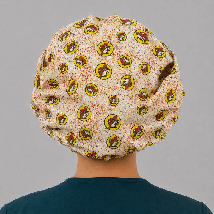 Beaver print bouffant scrub cap for women, front view, cartoon beaver mascot in red and yellow badges on cream, handmade funny surgical hat by OR World