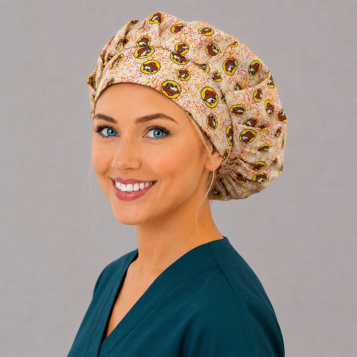 Beaver print bouffant scrub cap left three-quarter angle on smiling model showing red and yellow beaver mascot badges on cream, women&