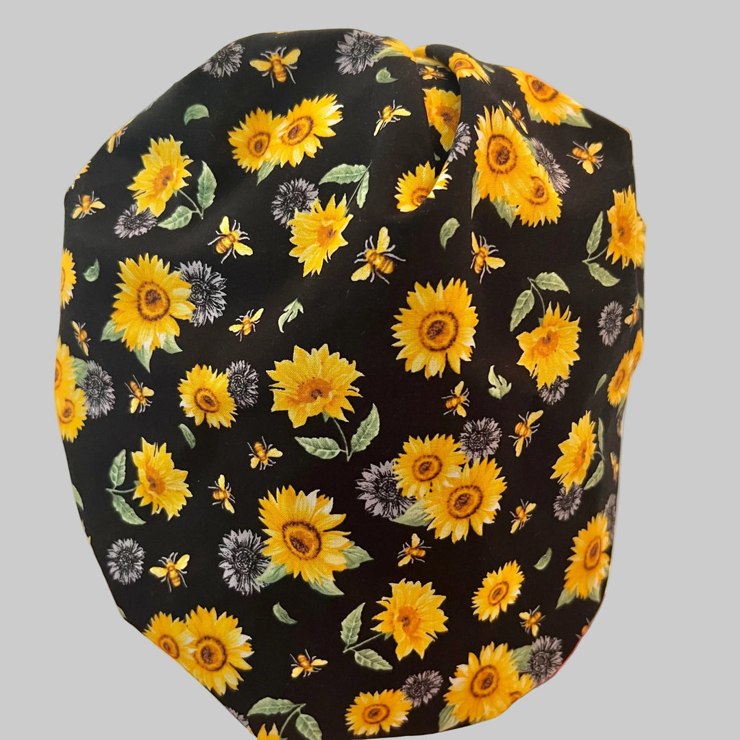 Bee Grateful bouffant scrub cap with golden sunflowers & honeybees on black, front view — handmade-in-USA surgical hat for women from OR World.