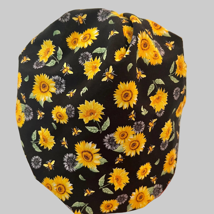 Bee Grateful bouffant scrub cap with golden sunflowers &amp; honeybees on black, front view — handmade-in-USA surgical hat for women from OR World.