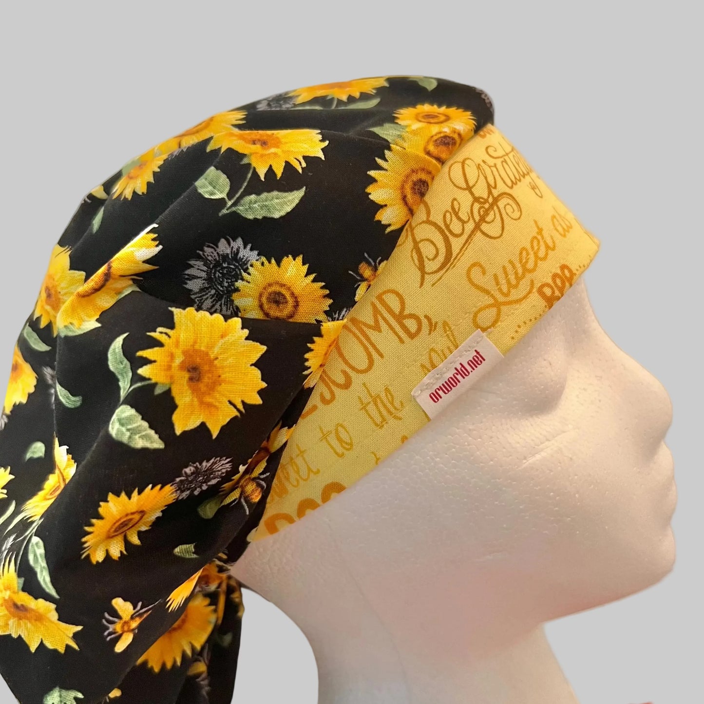 Side view of Bee Grateful sunflower & bee bouffant scrub cap with yellow script band — handmade USA surgical hat for OR nurses with room for long hair.