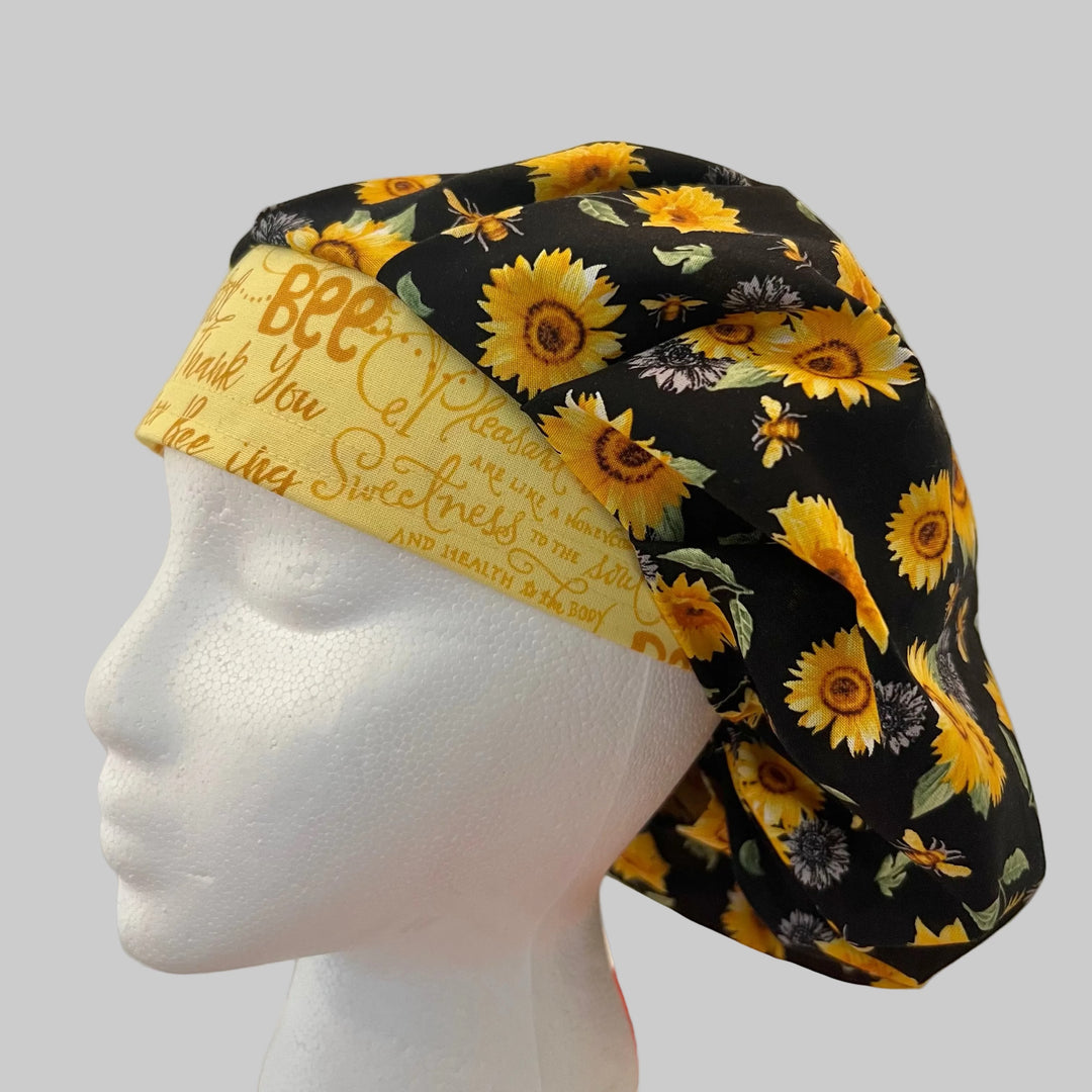Top view of Bee Grateful sunflower &amp; honeybee bouffant scrub cap fabric on black — handmade-in-USA OR World surgical hat for women.