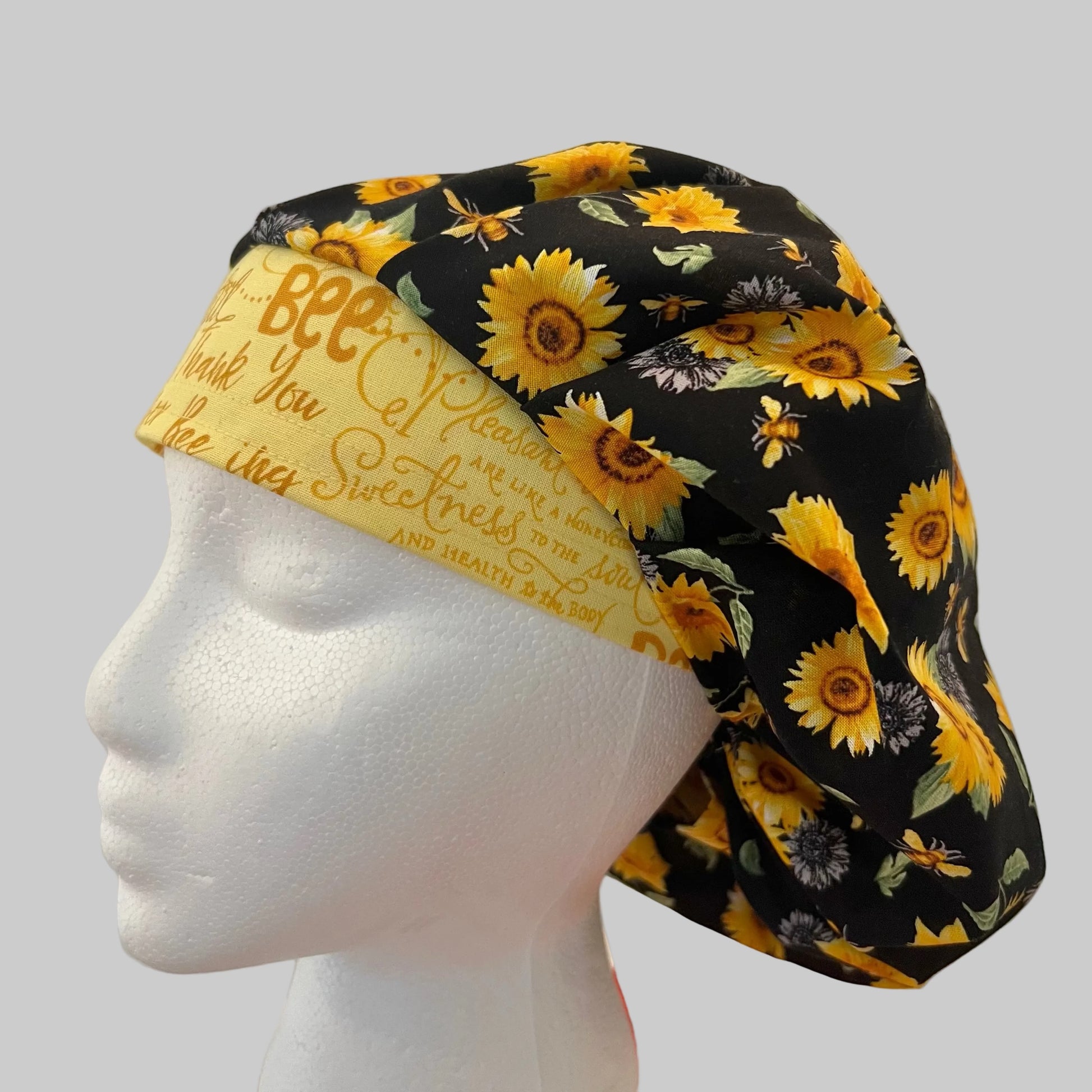 Top view of Bee Grateful sunflower & honeybee bouffant scrub cap fabric on black — handmade-in-USA OR World surgical hat for women.