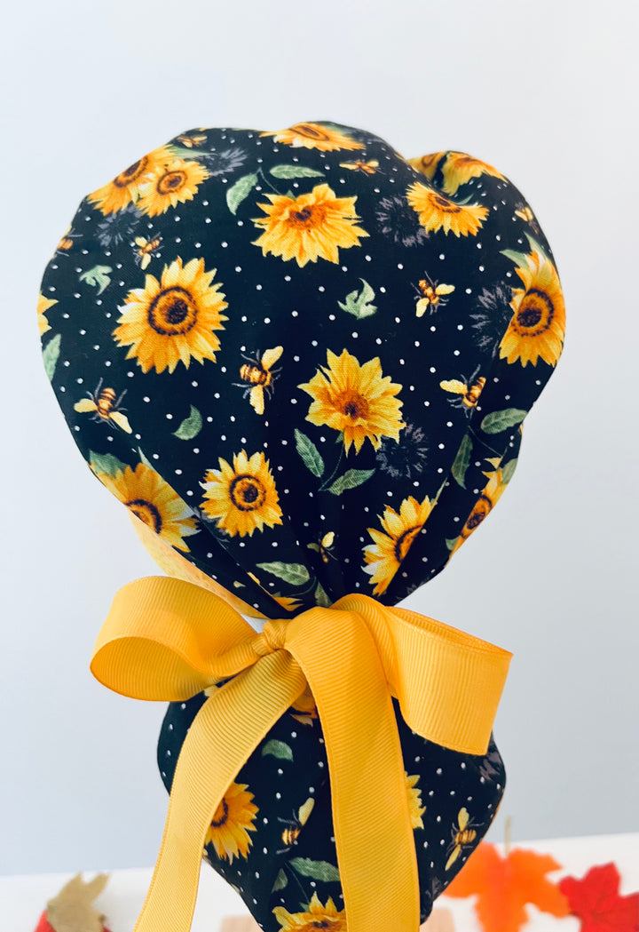 Back view of Bee Grateful sunflower ponytail scrub cap with yellow bow and ponytail pouch — handmade-in-USA OR World surgical hat for long hair.