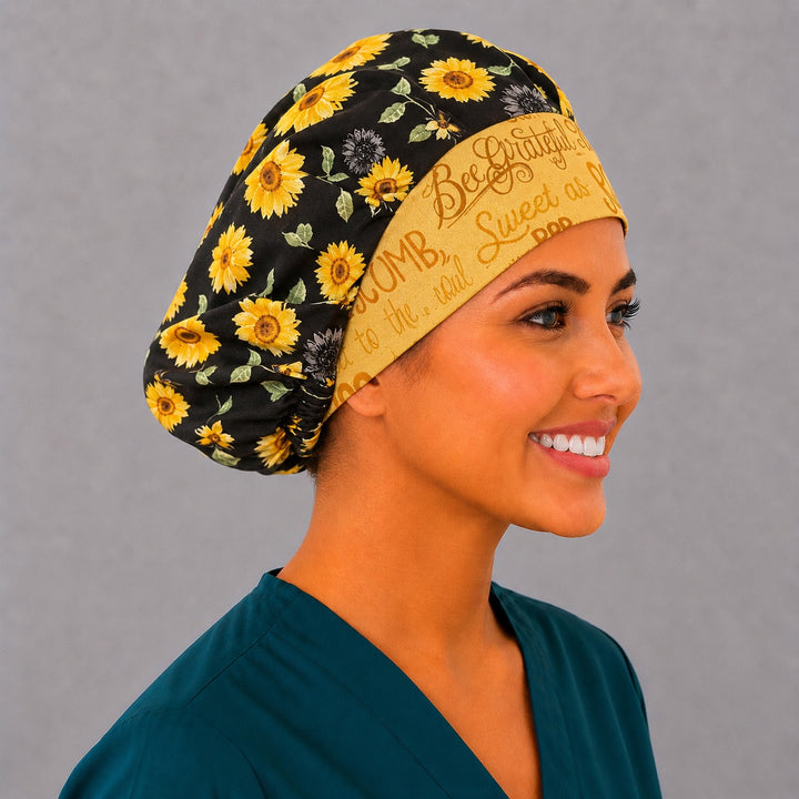 Bee Grateful sunflower bouffant scrub cap left three-quarter angle on smiling model showing golden sunflowers, honeybees and yellow script band, OR World nurse hat