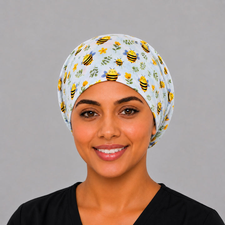 Bee Happy Blooms Euro scrub cap with cartoon honeybees &amp; flowers on light blue, front view on a model — handmade-in-USA surgical hat for women from OR World.