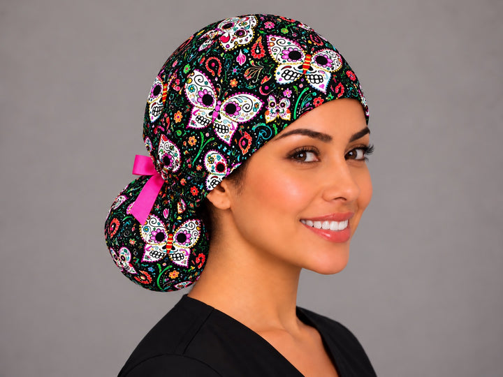 Three-quarter view of the black paisley sugar skull ponytail nurse cap on a smiling OR nurse, low bun held in the printed pouch