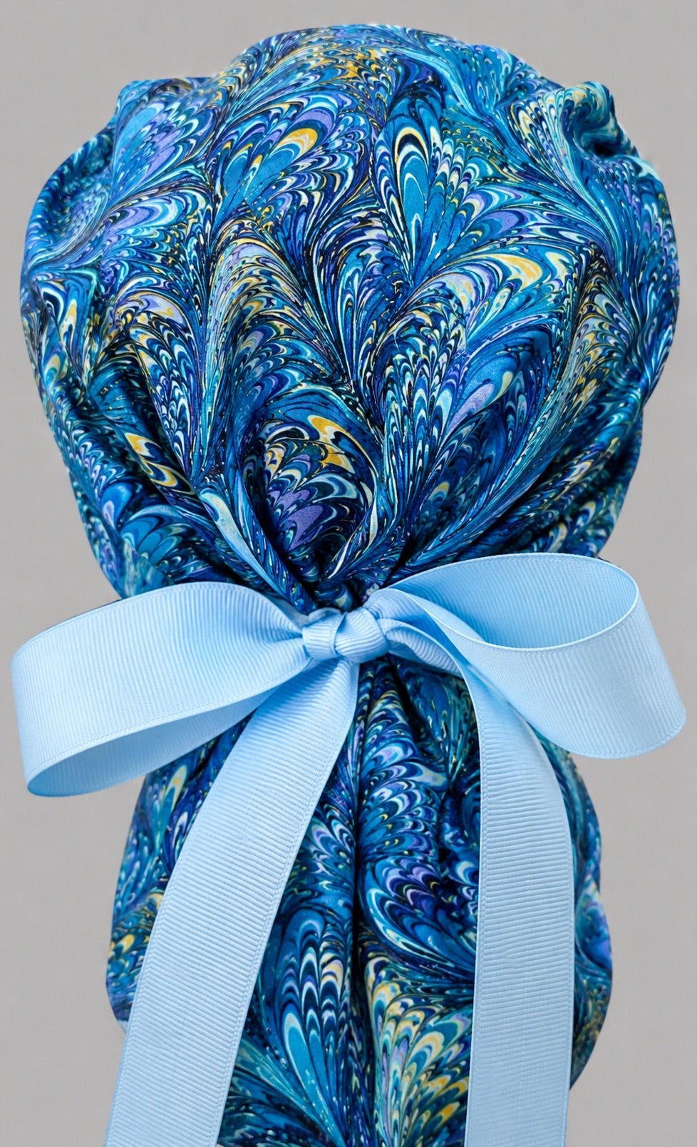 Blue marble ocean swirl ponytail scrub cap back view close-up showing gathered pouch full of blue, turquoise and gold marbled feather swirls and light blue ribbon bow