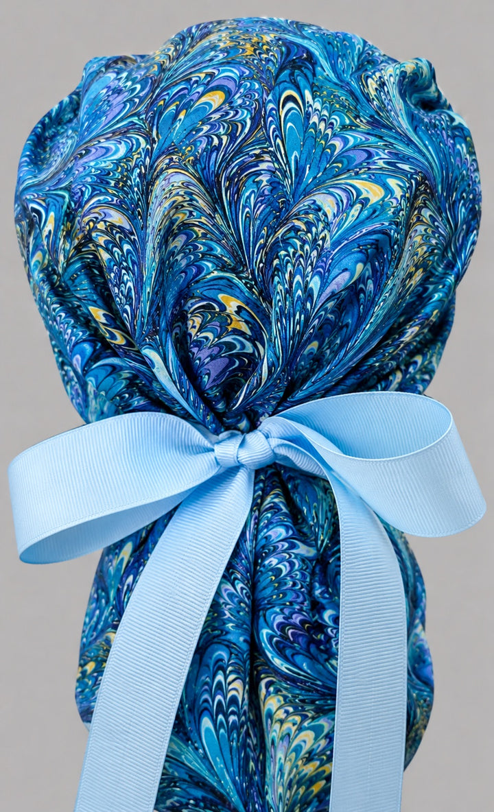 Blue marble ocean swirl ponytail scrub cap back view close-up showing gathered pouch full of blue, turquoise and gold marbled feather swirls and light blue ribbon bow