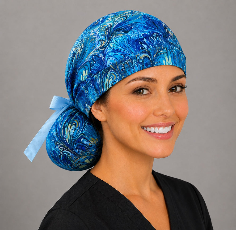 Blue marble ocean swirl ponytail surgical cap left three-quarter angle showing gathered ponytail pouch of blue and gold marbled swirls and light blue grosgrain ribbon bow