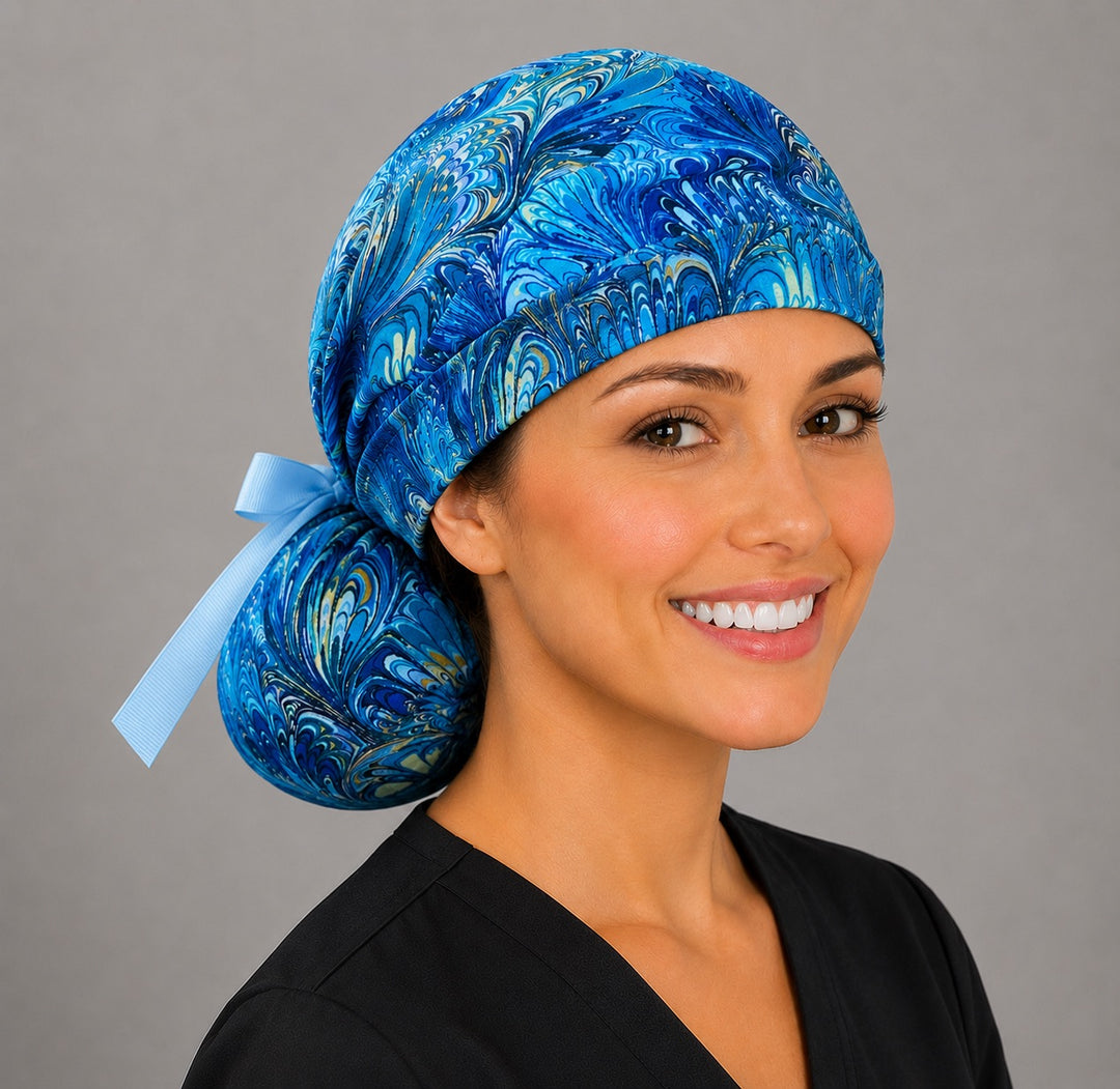 Blue marble ocean swirl ponytail surgical cap left three-quarter angle showing gathered ponytail pouch of blue and gold marbled swirls and light blue grosgrain ribbon bow