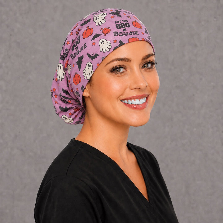 Woman wearing an I Put The Boo In Boujie Euro scrub cap, front view — pink ghosts, pumpkins and bats, adjustable Halloween surgical hat