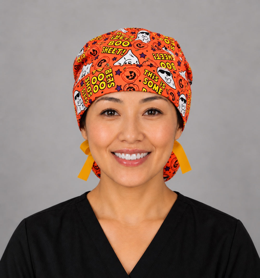 Woman wearing a Boo Sheet ghost ponytail scrub cap, front view — funny ghosts and pumpkins on orange, adjustable Halloween surgical hat