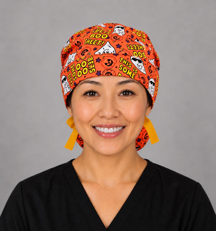 Woman wearing a Boo Sheet ghost ponytail scrub cap, front view — funny ghosts and pumpkins on orange, adjustable Halloween surgical hat