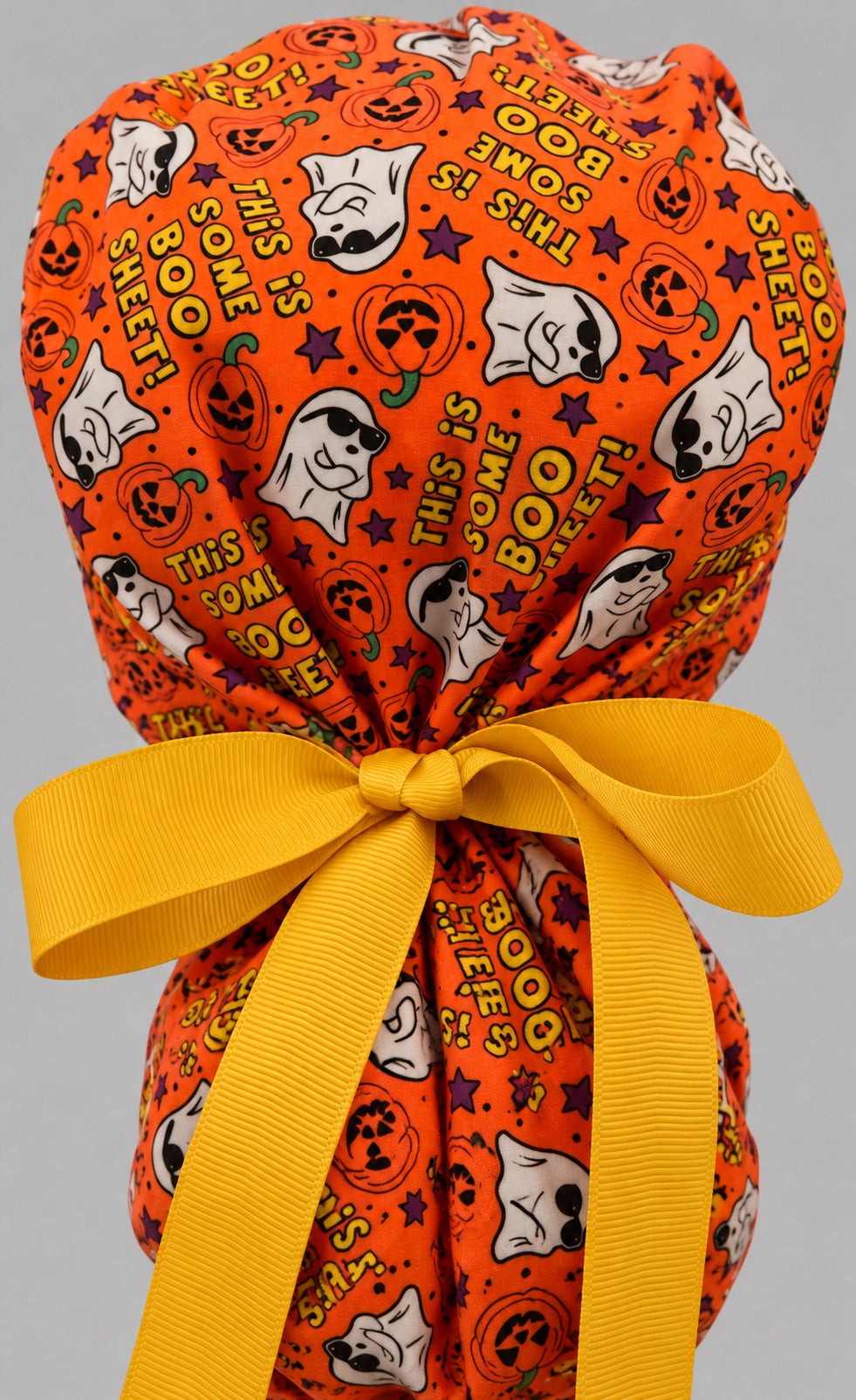 Back view of the Boo Sheet ponytail scrub cap — golden yellow grosgrain bow tied over the pouch with ghosts and lettering