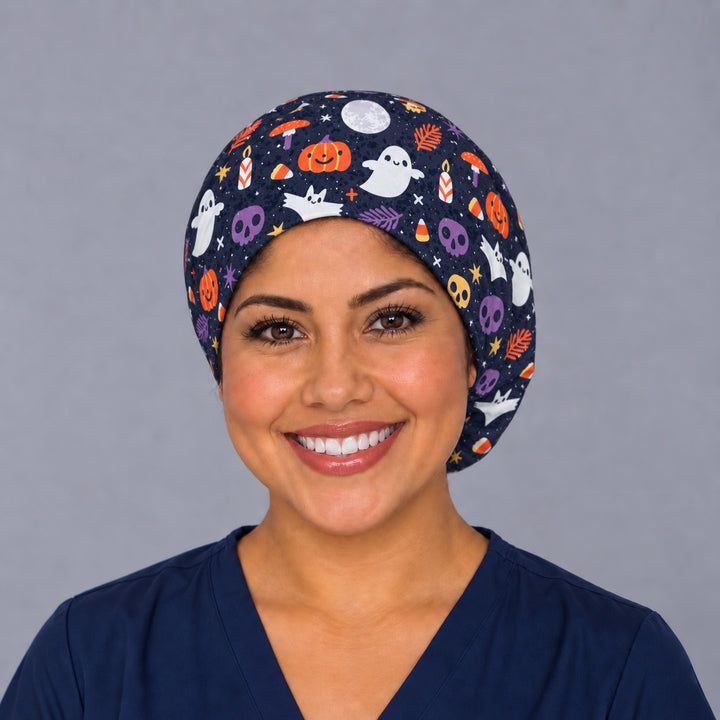 Woman wearing a Boo-tiful Harvest Euro scrub cap, front view — ghosts and pumpkins on navy, adjustable Halloween surgical hat