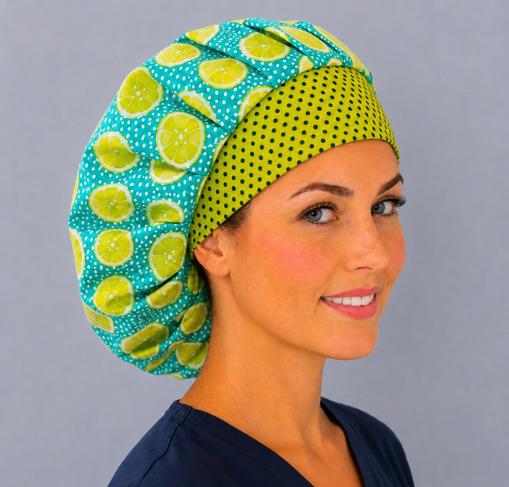Angled view of the bright citrus fruit bouffant scrub cap on a smiling vet tech — lemon lime print surgical cap, one size fits most