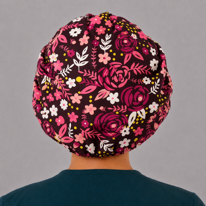 Back view of the brown floral bouffant scrub cap — full roomy fit with hot pink and red roses, daisies and leaves on a deep black print