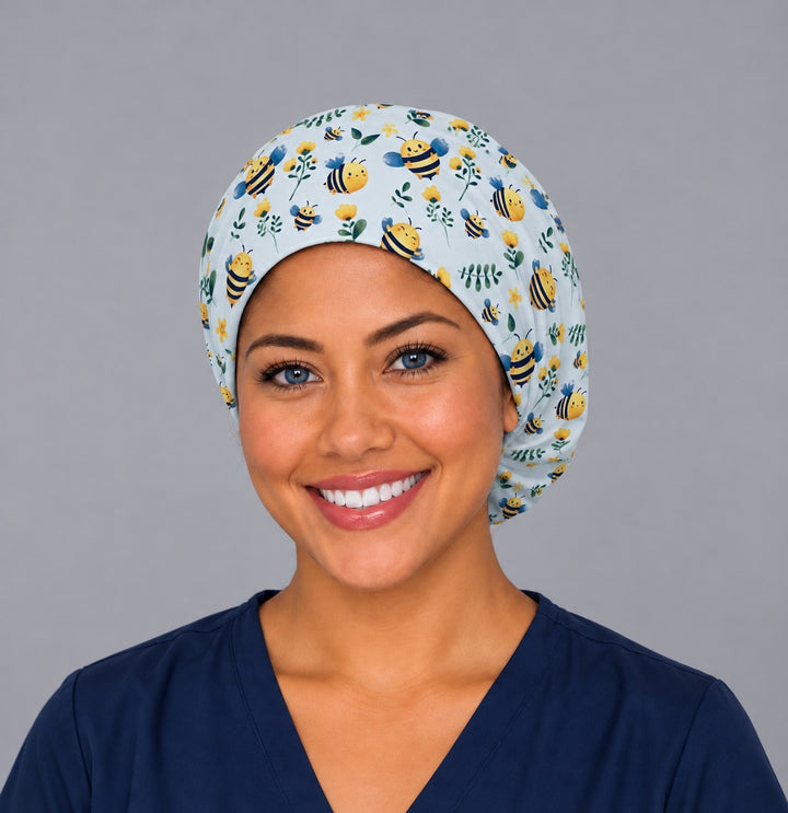 Smiling nurse in navy scrubs wearing a bumble bee euro scrub cap, front view of the powder blue bee and yellow flower print framing the forehead