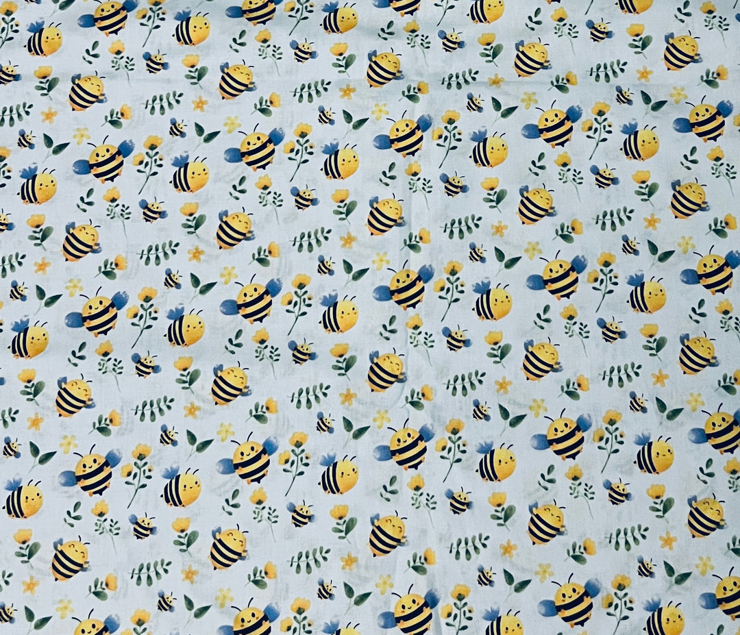 Close-up of the bumble bee cotton fabric, with chubby smiling bees, yellow blossoms and green leaves scattered on pale blue