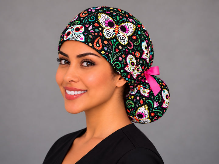 Butterfly calavera ponytail surgical hat for long hair with a hot pink bow at the bun, fuchsia and turquoise mariposa skulls on black cotton