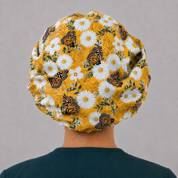 Back view of the butterfly and daisy bouffant scrub cap — full gathered fit showing monarchs and white daisies across the mustard crown