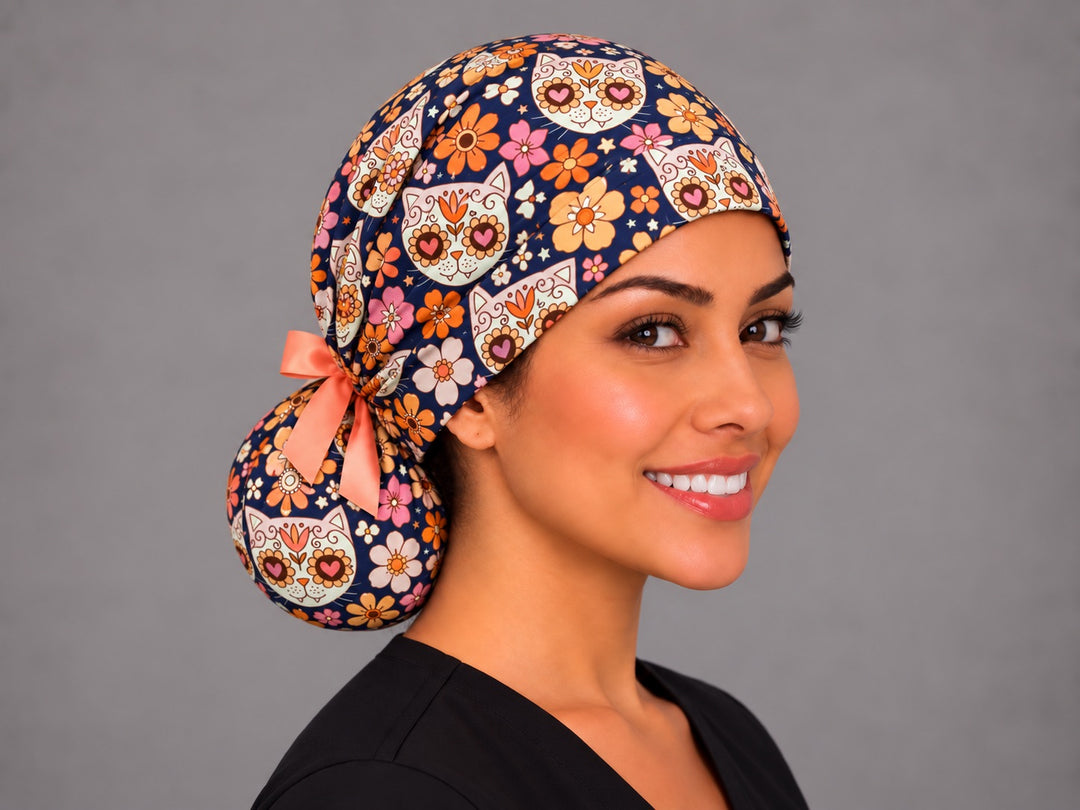 Calavera cat ponytail surgical hat for long hair with a peach satin bow at the bun, retro orange and pink flowers on navy cotton
