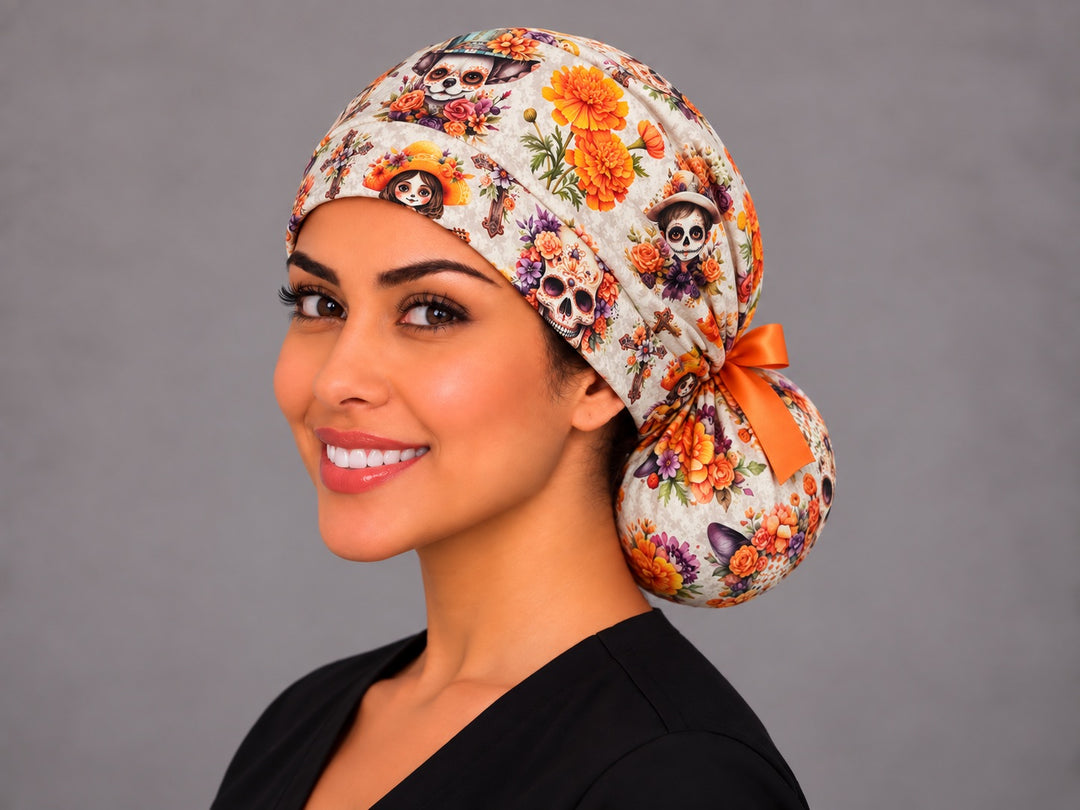 Three-quarter view of the calavera ponytail surgical hat for long hair, orange satin bow tied at the bun, cempasúchil and catrina print on cream