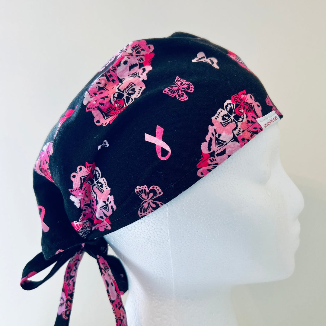 Side view of cancer hearts butterfly scrub cap with pink awareness ribbon, handmade tie-back surgical hat on black