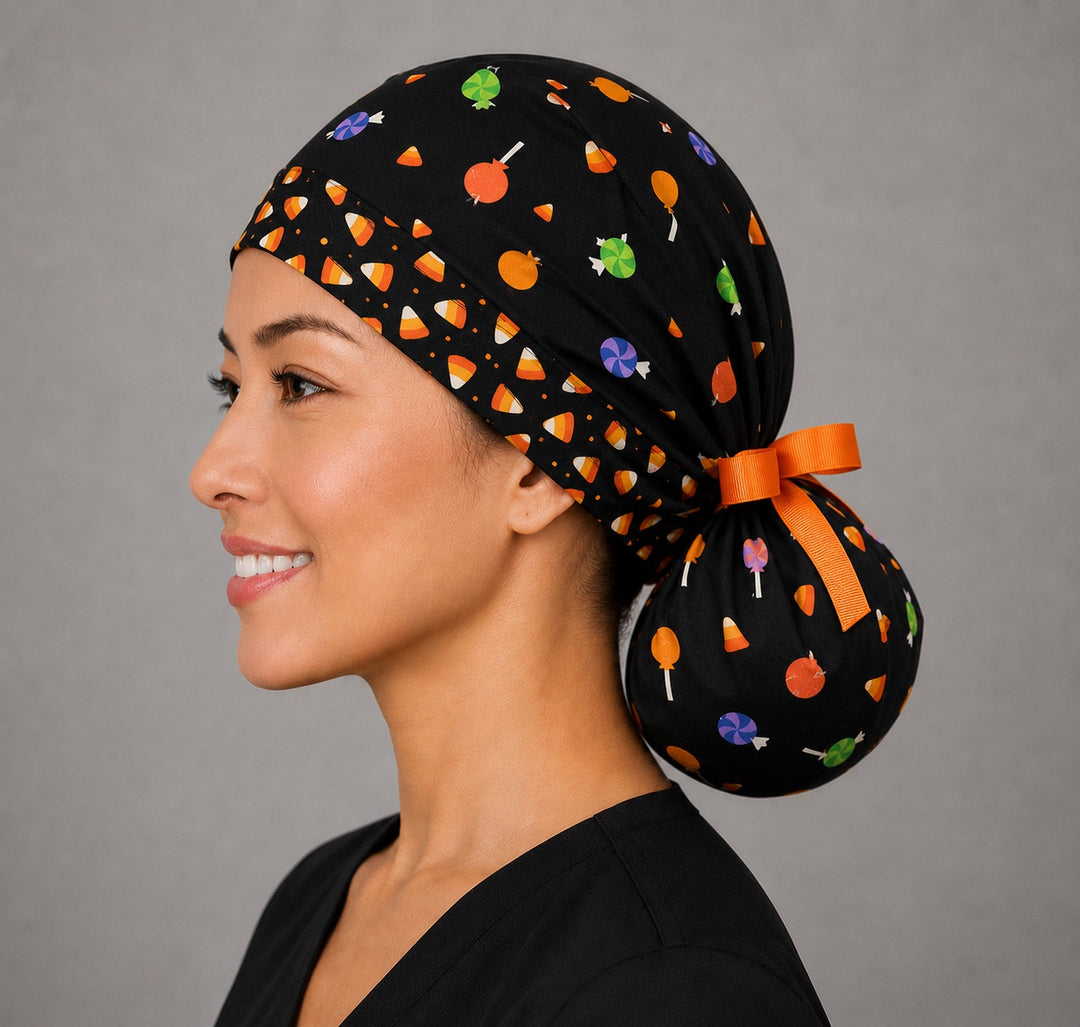 Halloween candy corn ponytail scrub cap back view close-up showing gathered pouch full of candy corn, lollipops and wrapped candy on black with orange grosgrain ribbon bow