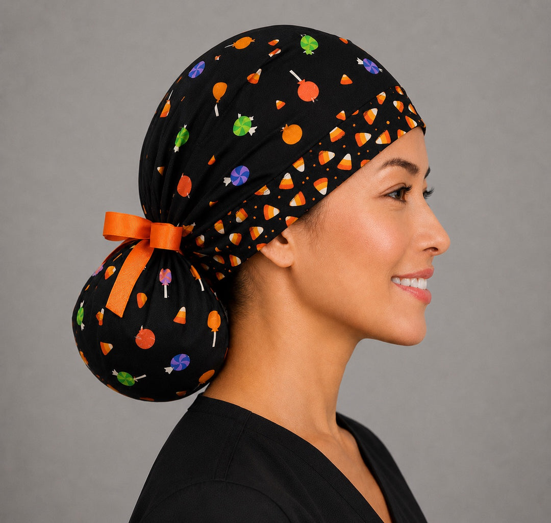 Woman wearing Halloween candy corn ponytail scrub cap, front view smiling with candy corn, lollipops and wrapped candy on black with orange ribbon tie