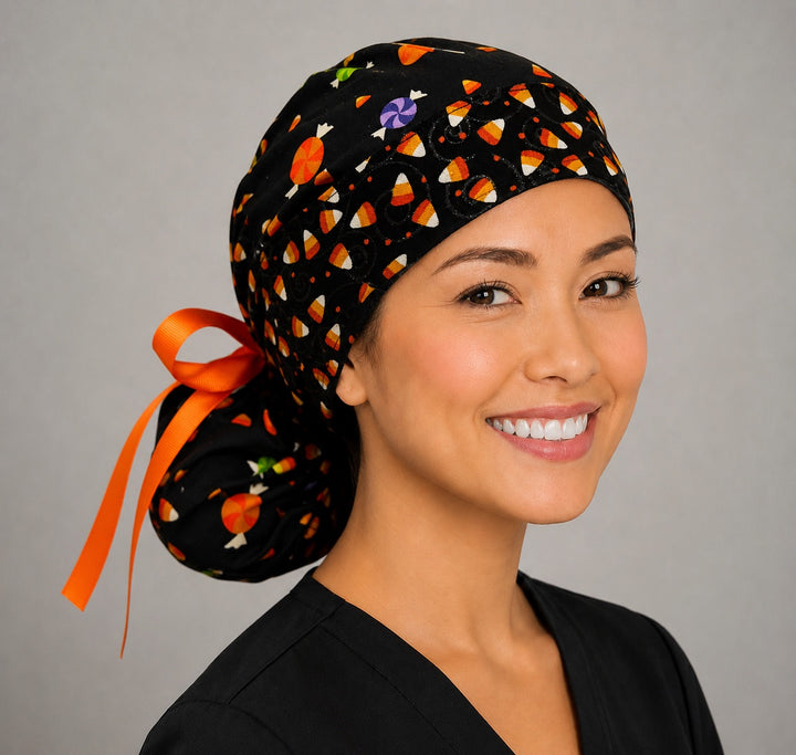 Halloween candy corn ponytail scrub cap right side profile showing gathered ponytail pouch of candy corn, lollipops and candy on black with orange ribbon tie