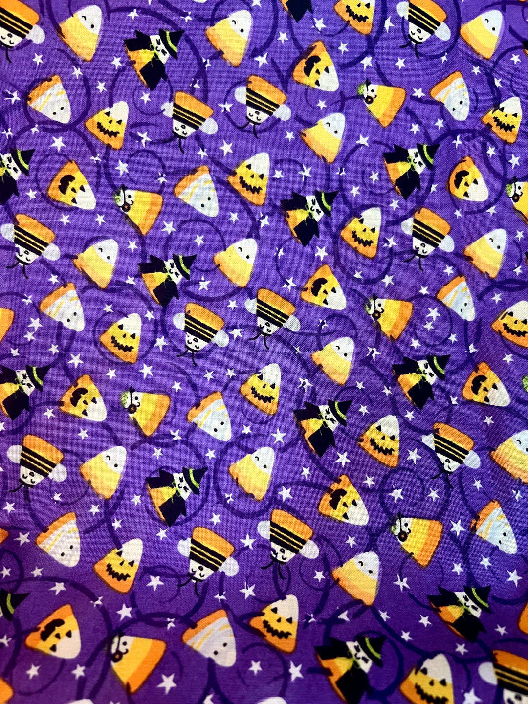 Fabric detail of the candy corn witches scrub cap — close-up of candy corn characters and witch hats on purple cotton
