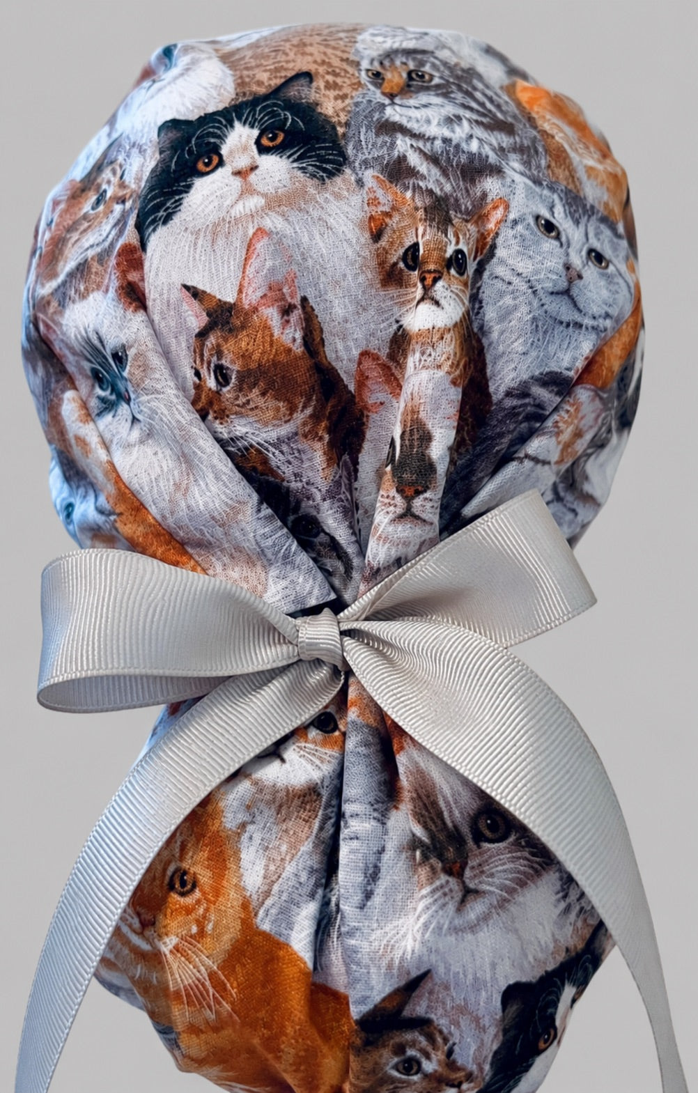 Woman wearing cats and kittens ponytail scrub cap, front view smiling with photorealistic cat collage print and gray ribbon tie