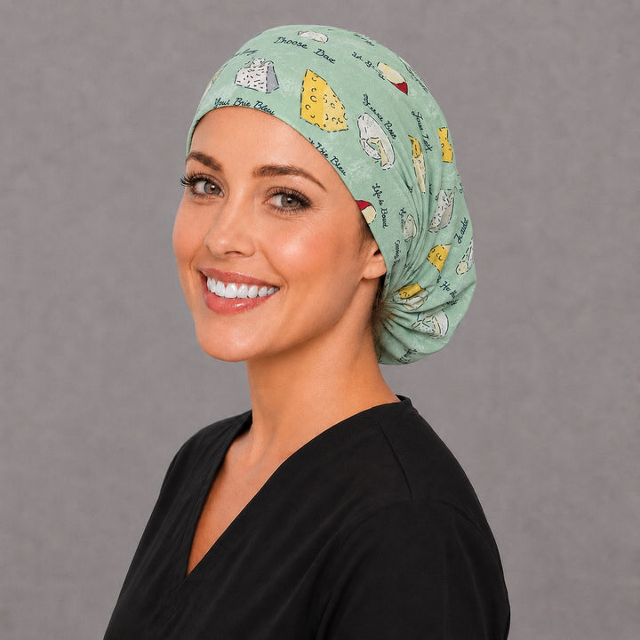 Woman wearing a cheese lover Euro scrub cap, front view — cheese wedges and puns on sage green, adjustable surgical hat for nurses