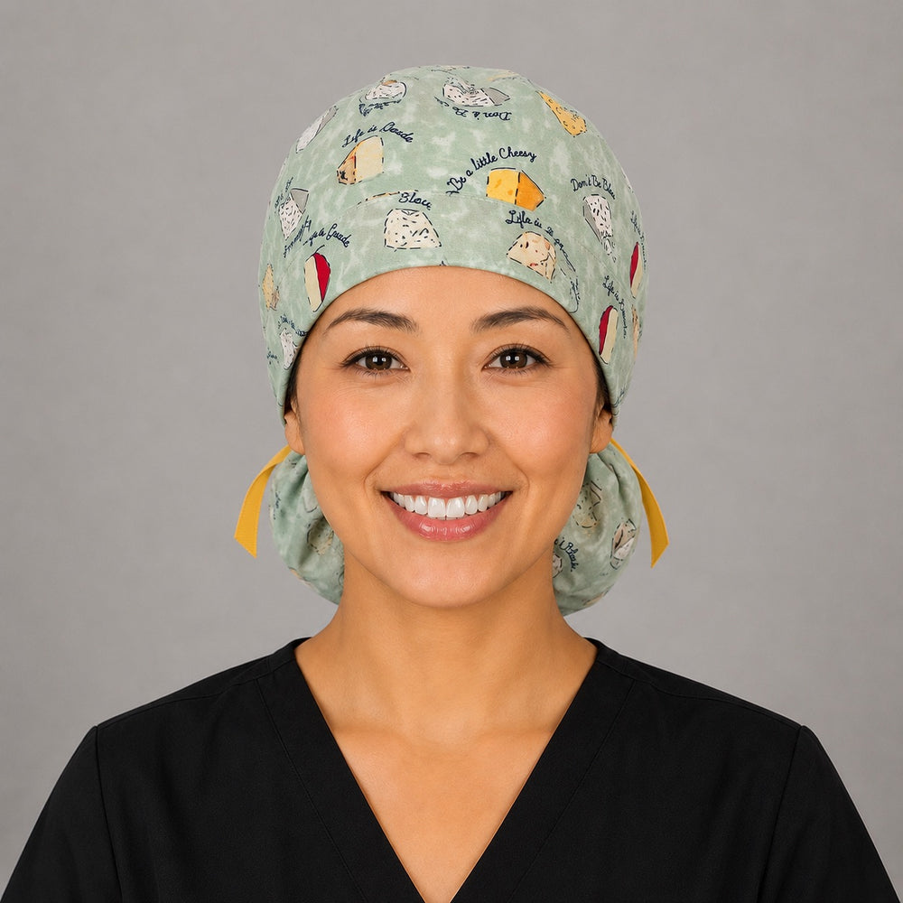 Woman wearing funny cheese pun ponytail scrub cap, front view smiling with cheese wedges, Life is Gouda sayings on sage green and yellow ribbon tie