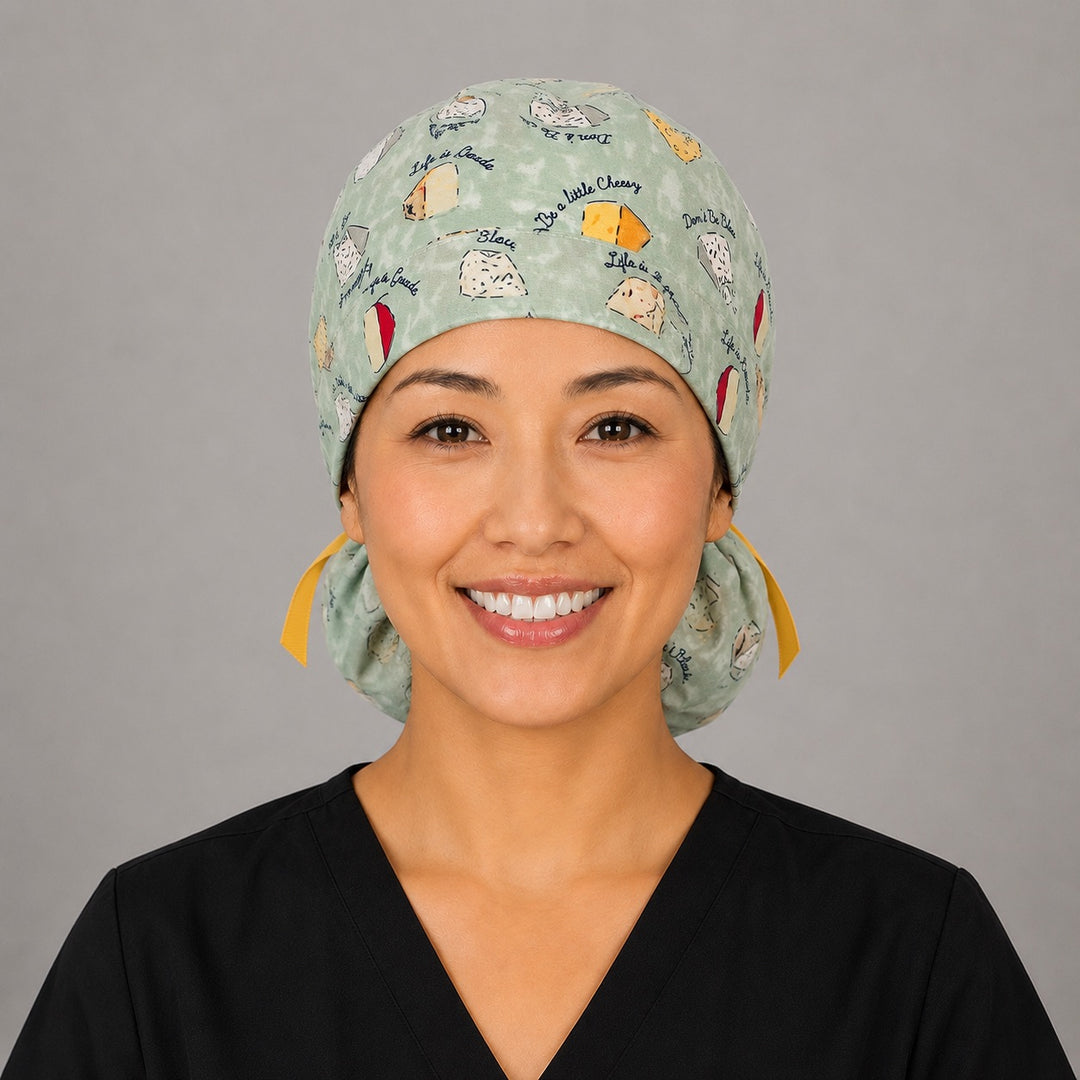 Woman wearing funny cheese pun ponytail scrub cap, front view smiling with cheese wedges, Life is Gouda sayings on sage green and yellow ribbon tie