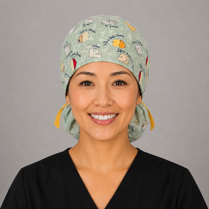 Woman wearing funny cheese pun ponytail scrub cap, front view smiling with cheese wedges, Life is Gouda sayings on sage green and yellow ribbon tie