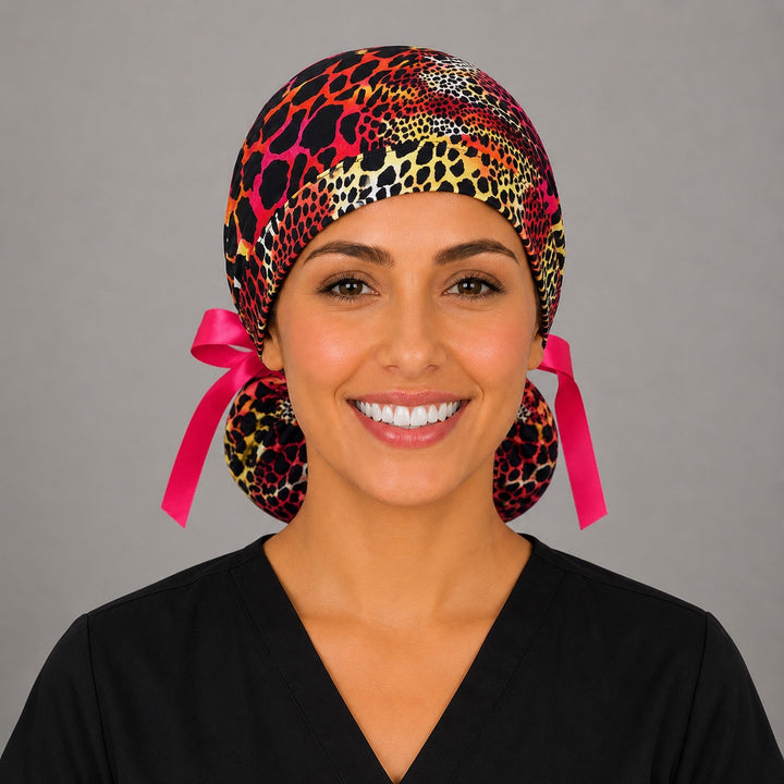 Woman wearing neon cheetah leopard ponytail scrub cap, front view smiling with pink, orange, yellow and black animal print and hot pink ribbon tie