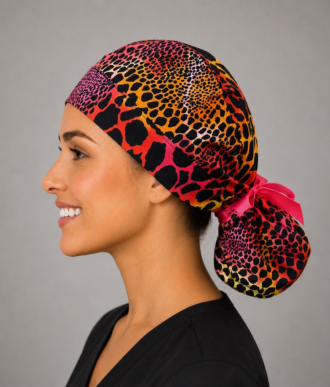 Neon cheetah leopard ponytail nurse cap left three-quarter angle on smiling model showing pink orange yellow animal print and hot pink ribbon bow